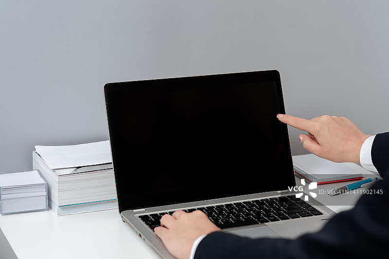 女商人在桌上的笔记本电脑键盘上打字，用一个手指指点重要的想法。办公室女性在电脑上写迟到的信息。图片素材