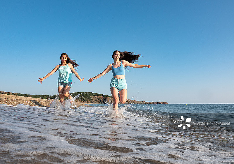 两个年轻快乐的女人享受在海滩上跑步和在浅水中制造水花图片素材
