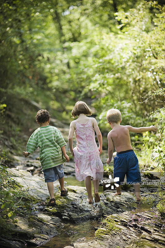 一个9岁的女孩，7岁的男孩和一个6岁的西班牙男孩在外面的小溪里玩耍和探索。图片素材