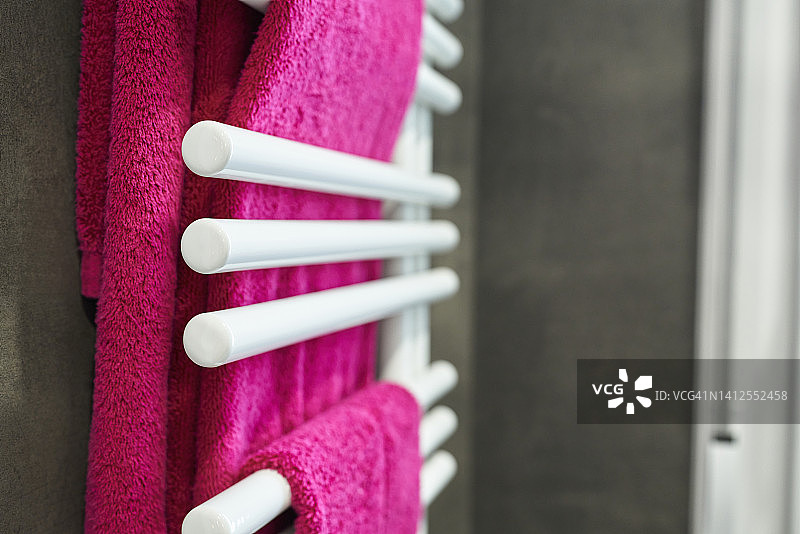 浴室内挂在壁挂式金属毛巾架上的紫红色毛巾的正面和侧面图片素材
