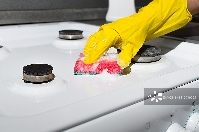 女工手戴手套，用洗涤海绵和化学泡沫清洁煤气炉表面。家庭清洁理念，厨房卫生图片素材
