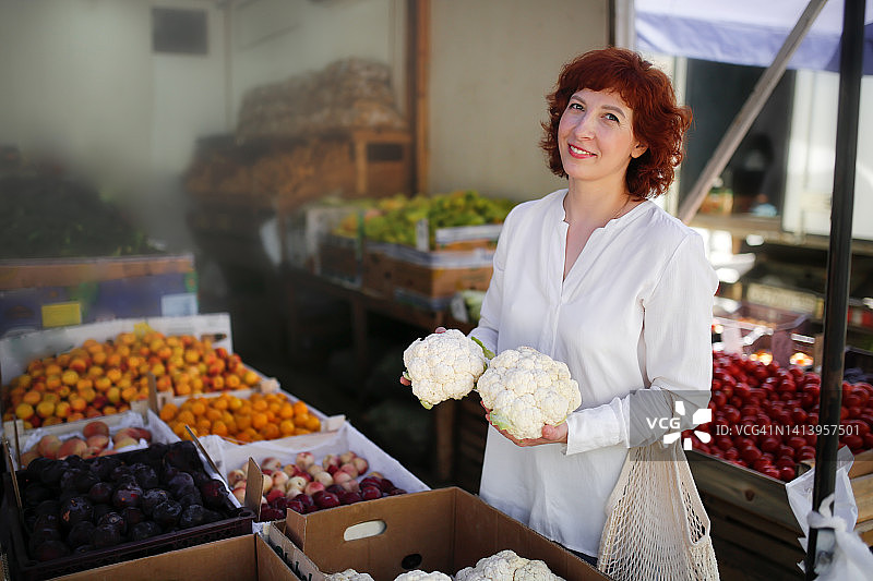 市场上的中年妇女用生态网袋选择菜花图片素材