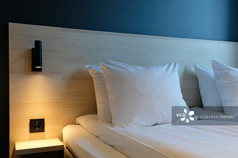 卧室的碎片与空床头柜，打开阅读灯和插座在现代室内设计的家庭或酒店。柔软的枕头和毯子，时尚舒适的家具。图片素材