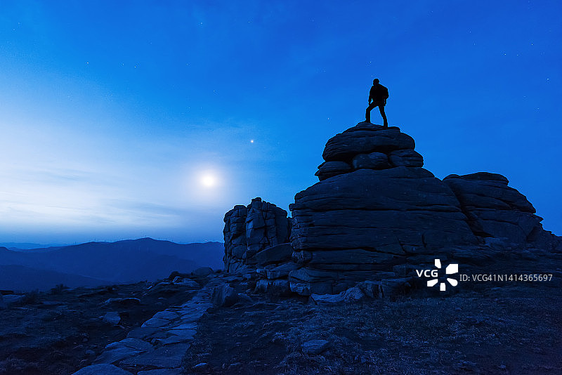 剪影摄影师在黎明前站在中国冰山梁上的巨石上图片素材