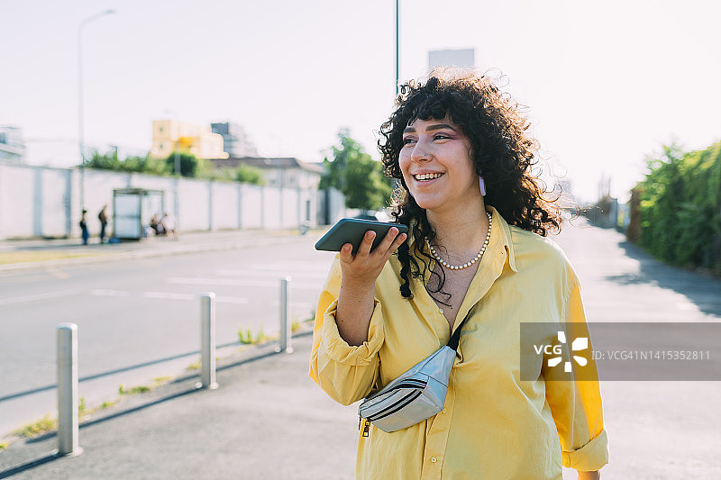微笑的女人在街上用智能手机发送语音信息图片素材