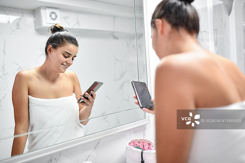 一名女性在洗澡后为晚上外出做准备时一边看手机短信图片素材