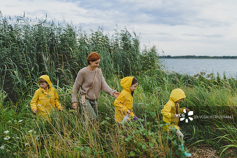 快乐的妈妈带着三个孩子在雨天户外，穿着黄色的雨衣。图片素材