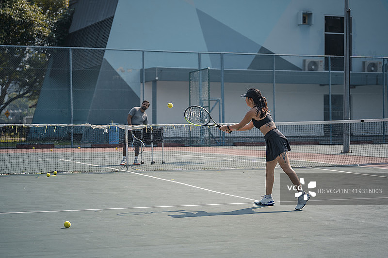 亚洲中国女网球运动员在周末的早上和她的教练在硬地场上练习图片素材