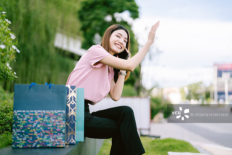 亚洲女性拿着购物袋微笑着坐在电话上。图片素材