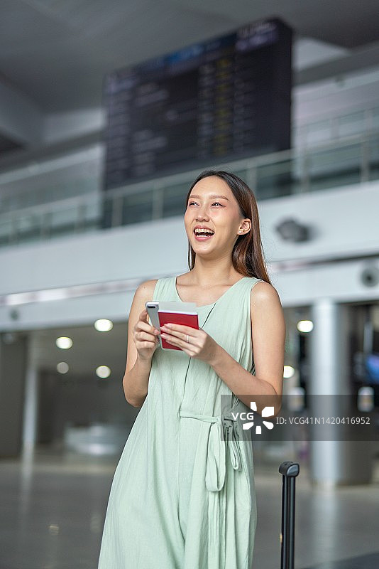 一个年轻的亚洲女性的肖像照片与她的手机和行李箱走过一个出发板去她的梦想的度假目的地旅行图片素材