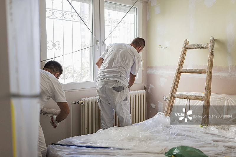 男人在家里的散热器周围刷墙图片素材