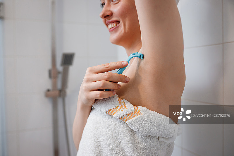 特写的女人剃腋毛用剃刀在淋浴间。在浴室进行脱毛手术图片素材