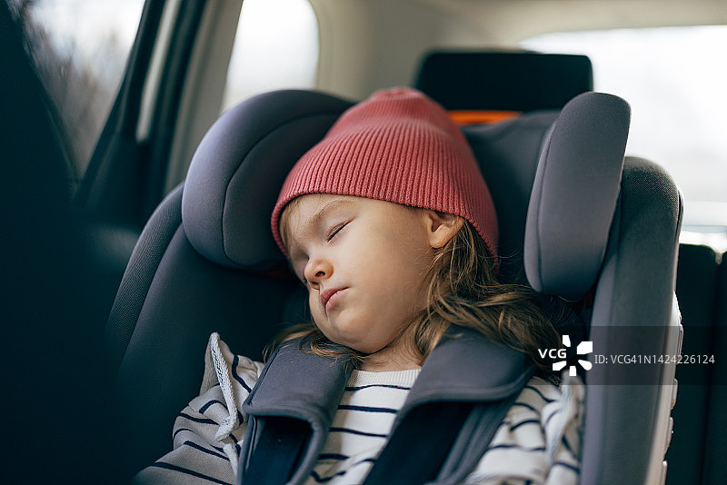 一个戴着红帽子的可爱小女孩在开车旅行时打盹的肖像图片素材