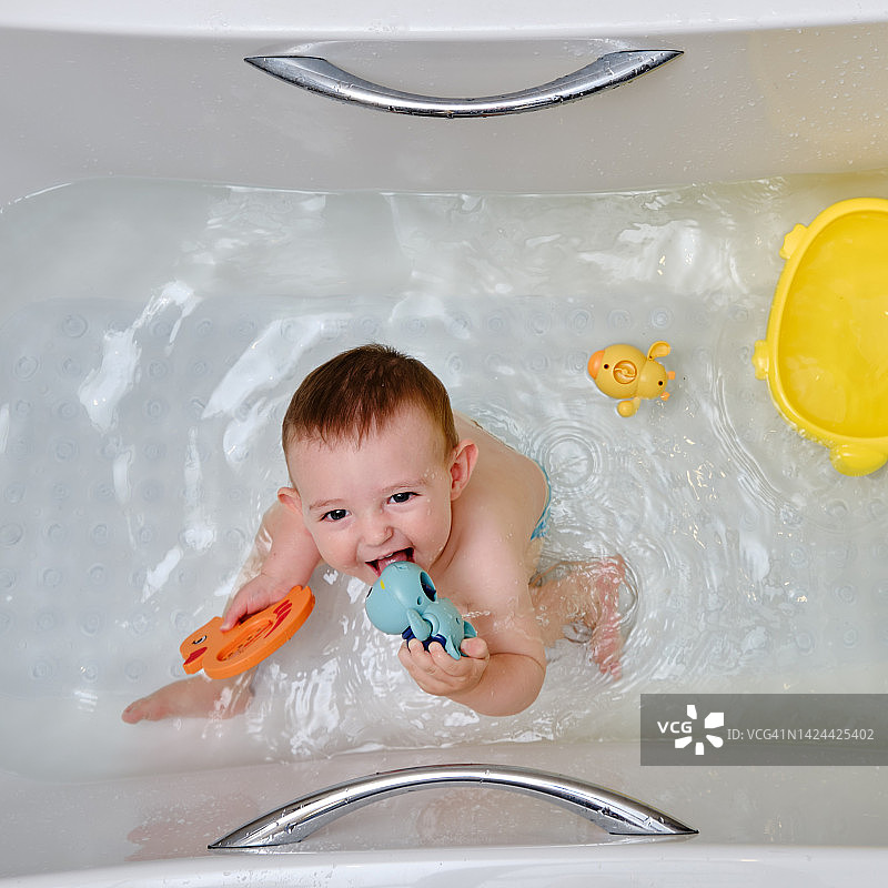 快乐的蹒跚学步的小男孩正在浴缸里玩玩具。一个微笑的孩子在家庭浴室的水里玩耍图片素材