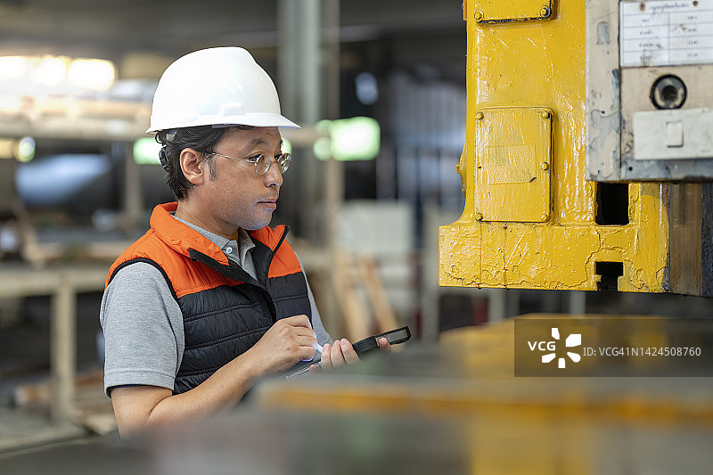 在制造工厂工作的日本工程师使用数字平板电脑检查重型机器的功能。图片素材