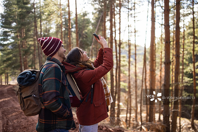 在阳光明媚的日子里，一名年轻女子和男友一起徒步旅行，用智能手机拍下了大自然的照片图片素材