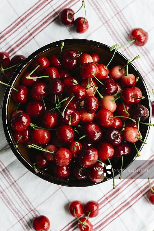 头顶上的新鲜樱桃在陶瓷碗上的红色条纹餐巾-有机水果的概念图片素材