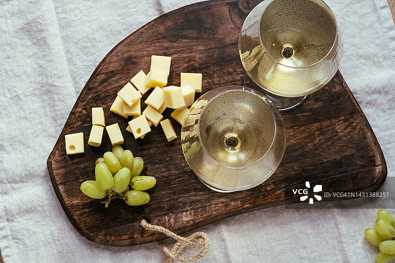 两杯白葡萄酒，奶酪和葡萄放在木板上图片素材