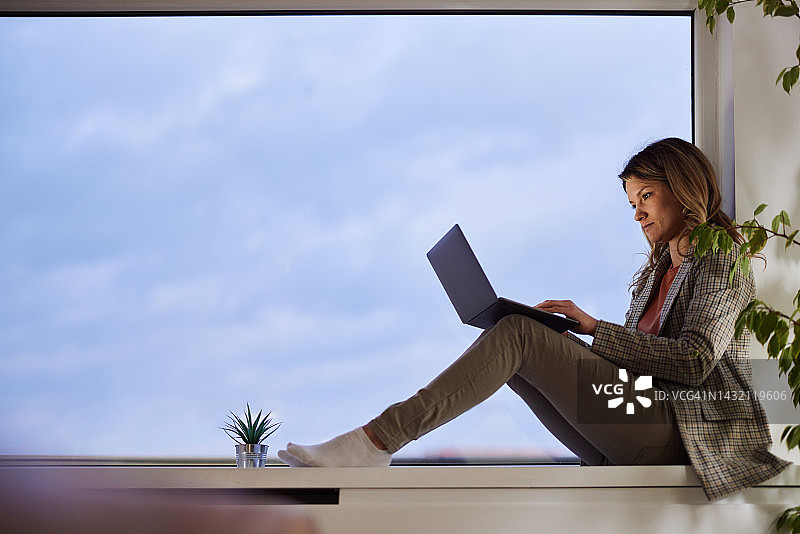 女企业家在窗边用笔记本电脑工作。图片素材
