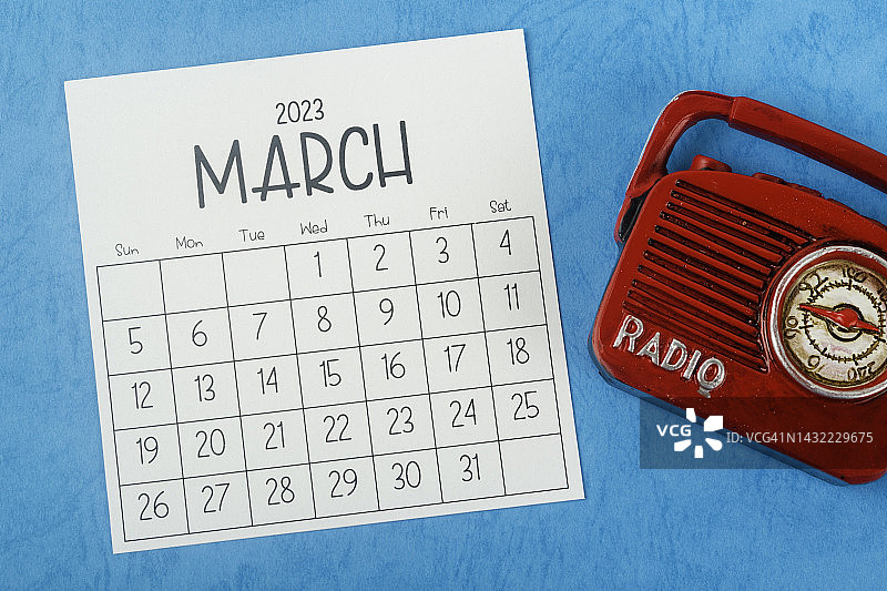 2023日历台:3月是组织者在蓝纸背景下用老式收音机计划和截止日期的月份。图片素材