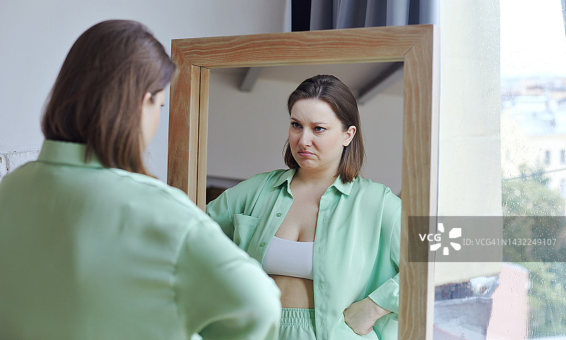 年轻胖女人照镜子会对自己的外表或超重感到沮丧和不满图片素材