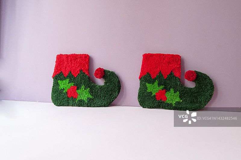 圣诞装饰件，用圣诞老人精灵的袜子或靴子制成的纺织地毯，来装饰家里，在淡粉色的背景上横视图片素材
