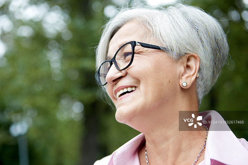 特写画像迷人的白发快乐老妇人戴着眼镜站在夏日公园，侧视脸图片素材