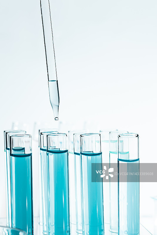 实验室玻璃器皿与滴管滴液体到试管浅蓝色液体近距离微距摄影。图片素材