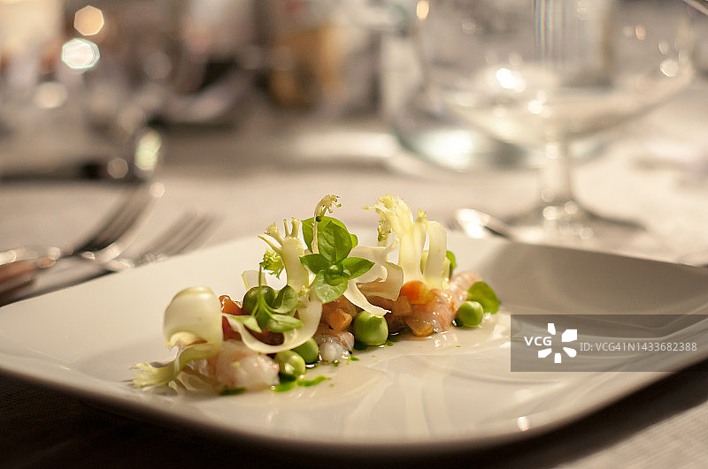 主菜是绿叶蔬菜和海鲜，放在背景模糊的白色瓷盘上图片素材
