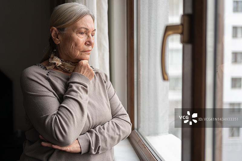 孤独的老年妇女透过窗户看图片素材