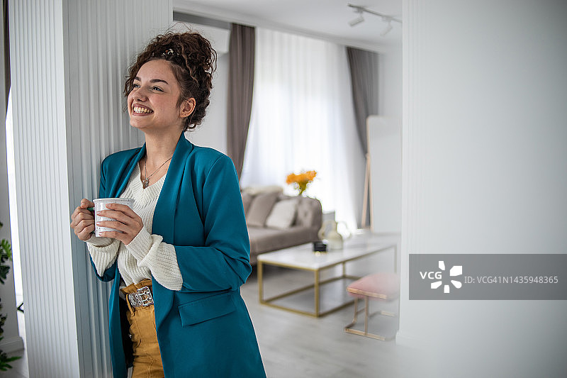 一个快乐的年轻女人在家里喝着咖啡图片素材