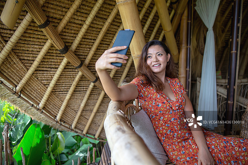 美丽的亚洲女子在竹制度假别墅里视频通话图片素材