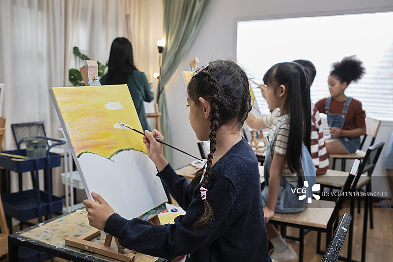 在美术工作室，一群孩子在女老师的指导下学习丙烯酸颜料。图片素材