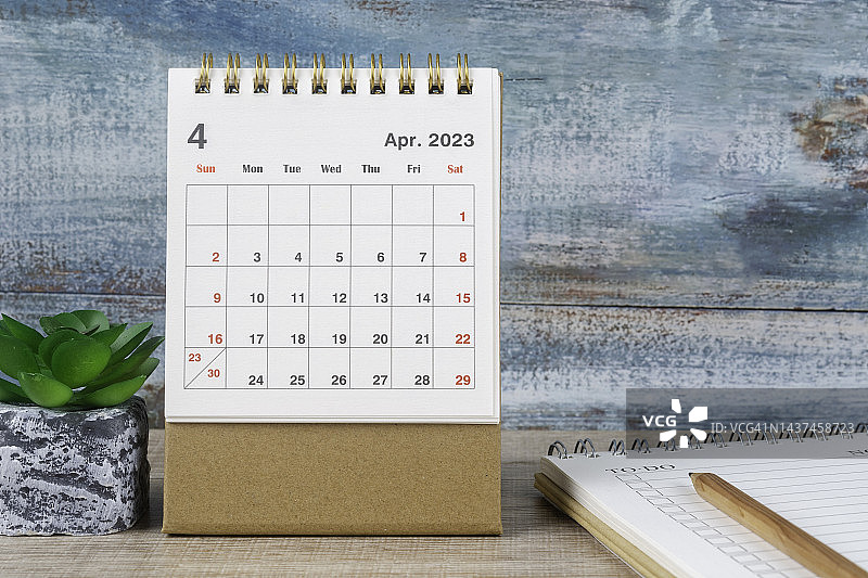 2023日历桌:4月是组织者计划的月份，最后期限是在旧木桌背景上放一盆室内植物和记事本。图片素材