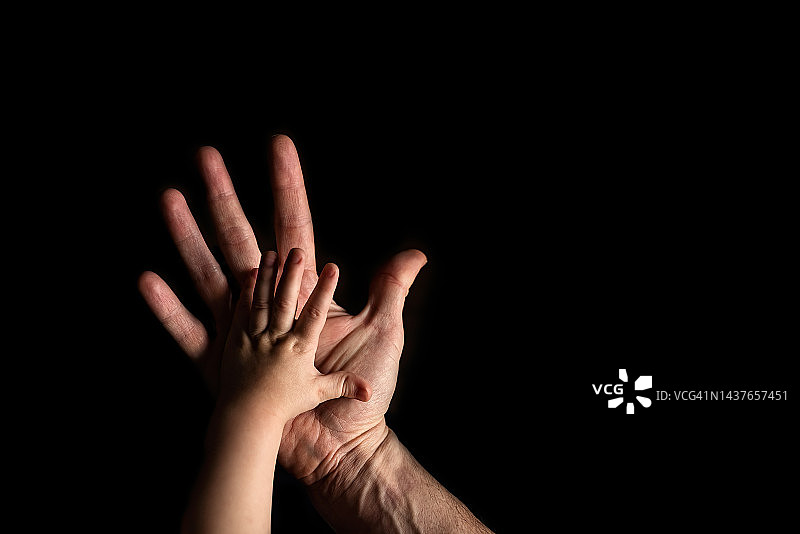 婴儿的手放在大人的手上，背景是黑色的图片素材