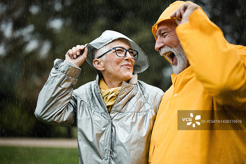 在公园里，一对快乐的成熟夫妇在雨天戴着头巾。图片素材