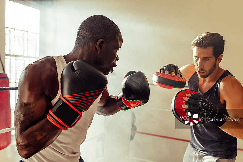 一个健壮的年轻人和他的拳击教练在健身房训练图片素材