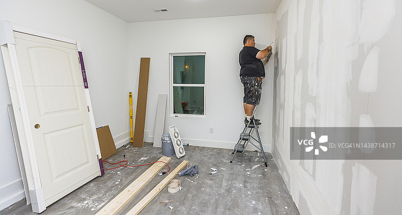 房子装修。一个白人修理工站在梯子上，用油灰把墙抹平。图片素材