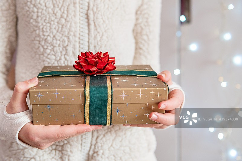 女性手拿白色毛衣，手持手工纸装饰的礼品盒。圣诞节的主题图片素材