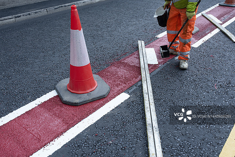 道路工人在新建沥青道路的白色、黄色和红色道路标记线上涂热熔交通耐漆图片素材