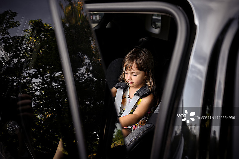 可爱的蹒跚学步的女孩坐在车内的安全座椅上。图片素材