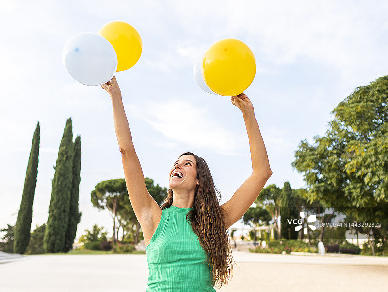 快乐的女人拿着黄色和白色的气球在人行道上图片素材