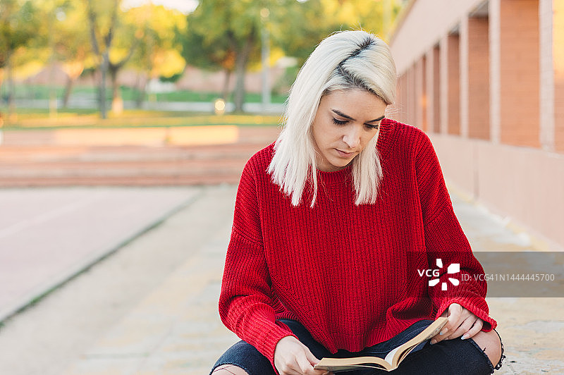 银发女孩坐着看书。穿着一件红毛衣。图片素材