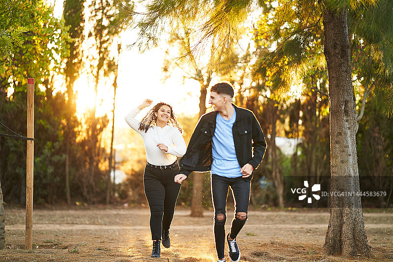 在日落时分，一对年轻的情侣微笑着在户外跑步和玩耍。图片素材