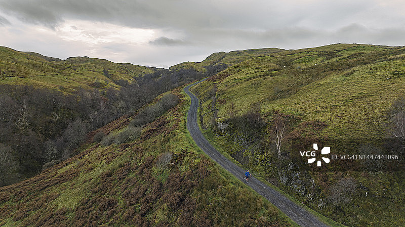 高架无人机拍摄的一名跑步者在苏格兰山区陡峭的砾石小道上图片素材