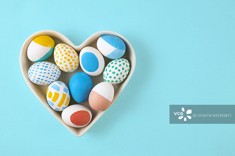 彩色复活节彩蛋在心形碗在蓝色背景图片素材