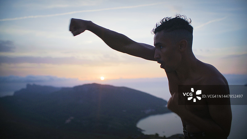 男运动员独自在悬崖上训练。练习拳击动作和出拳图片素材