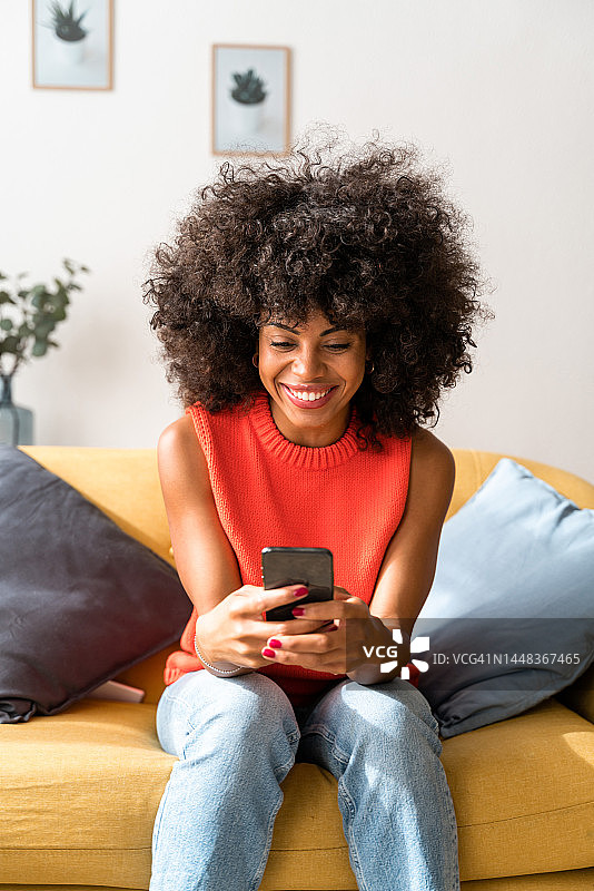 微笑的女人坐在客厅里，用手机发短信给她的朋友一起吃午饭。图片素材