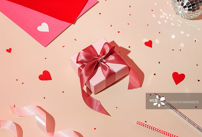 情人节构图理念:白色礼盒，品红色蝴蝶结，红心纸屑和粉彩背景的粉色纸。高角度视野，平铺图片素材