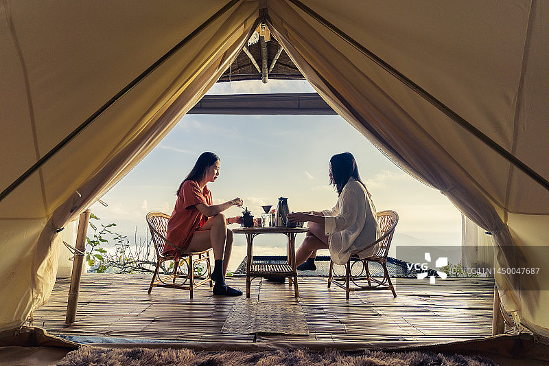 Two women sitting together making coffee with views of mountains, sea of ​​fog and sunlight. through tent view图片素材